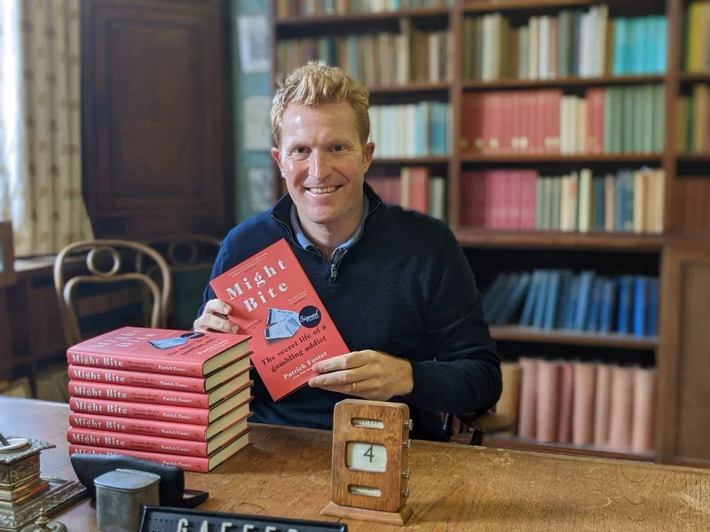 Patrick Foster sitting at a desk with a copy of his book, Might Bite